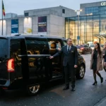 Chauffeur professionnel devant un Mercedes Classe V noir prêt à accueillir des passagers devant un complexe d'exposition