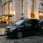 Mercedes Classe V noire avec chauffeur professionnel devant un lieu culturel à Bruxelles le soir