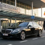 Berline premium attendant un passager devant un terminal d'aéroport en Belgique