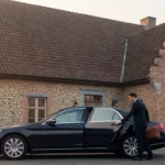 Chauffeur de taxi accueillant un passager devant une maison du Brabant wallon à l'aube